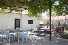 an outdoor patio with tables and chairs under a pergolated roof, surrounded by trees