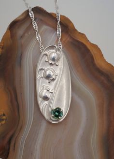 DEN2011 Lilly of the Valley sterling silver necklace. Lily of the Valley has a lot of meaning and symbolism, to us they represent spring: the end of winter and a new beginning. Their dainty bell-shaped flowers are unforgettable, their sweet scent is loved by all. This special piece features a Maine green tourmaline. Round brilliant cut gemstone is 4mm, approximately .25cts. Pendant measures approximately 32mmx15mm. Sold with an 18" sterling silver chain. This pendant can be special ordered in ye Retail Jewelry, End Of Winter, A New Beginning, New Beginning, Custom Jewelry Design, Green Tourmaline, Lily Of The Valley, Sterling Silver Necklace, Sterling Silver Chain