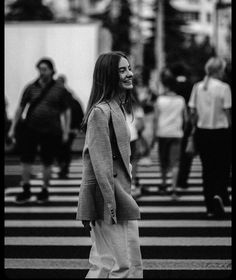 a black and white photo of a woman walking across a crosswalk with people in the background