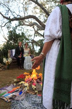 a woman standing in front of a fire with her hands on the ground and people sitting around