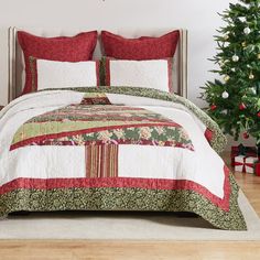 a bed with red and green comforter next to a christmas tree