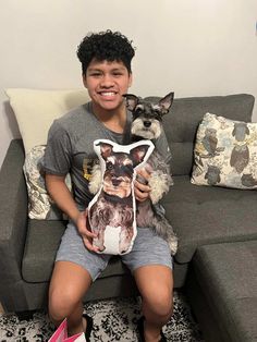 a boy sitting on a couch holding a dog pillow