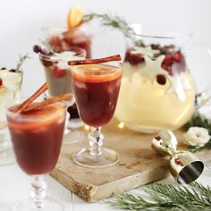 several glasses filled with drinks on top of a wooden cutting board next to evergreen branches