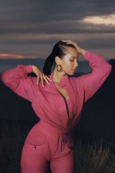 a woman in a pink jumpsuit posing for the camera with her hands on her head