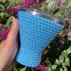 a hand holding a blue cup in front of purple flowers