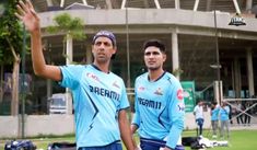 two men standing next to each other in front of a soccer field with their hands up