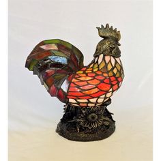 a stained glass rooster figurine sitting on top of a wooden base with a white background