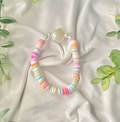 a multicolored beaded bracelet laying on top of a white sheet next to green leaves