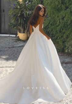 a woman in a white wedding dress standing on the sand with her back to the camera