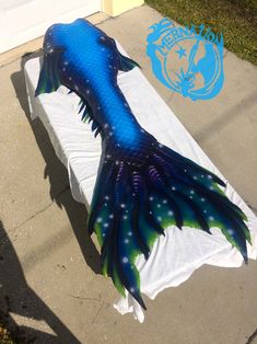 a large blue and green mermaid tail laying on top of a white sheet covered bench