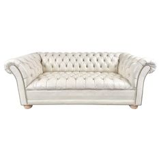 a white leather couch with buttons on the back and arms, in front of a white background