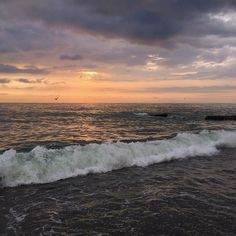 the sun is setting over the ocean with waves crashing in to shore and birds flying overhead