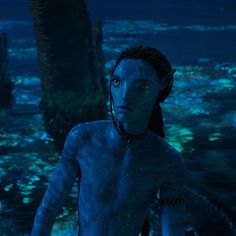 a man with blue paint on his body standing in front of a palm tree at night