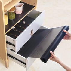 a person holding a roll of black paper in front of an open drawer with utensils on it