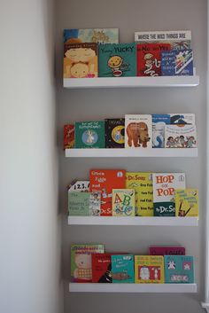 three white shelves filled with books on top of each other in front of a wall