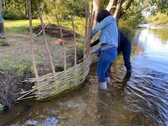 two people are standing in the water by some trees and branches that have been tied together