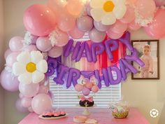 a birthday party with balloons, cake and flowers on the table in front of a window