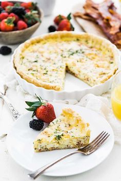 a white plate topped with a slice of quiche next to a bowl of fruit