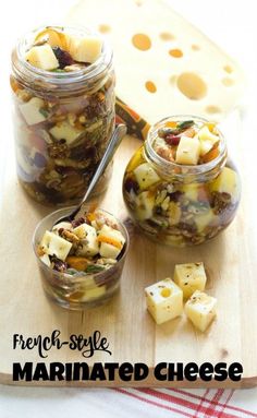 two jars filled with food sitting on top of a wooden cutting board next to cheese