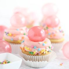 cupcakes with pink frosting and sprinkles on top, surrounded by balloons