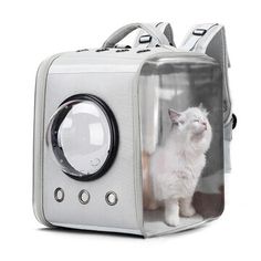 a white cat sitting inside of a clear case on the back of a backpack with its front door open