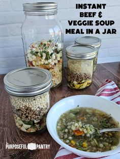 two mason jars filled with vegetables and soup on top of a wooden table next to a striped napkin