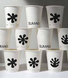 many cups with black designs on them are lined up against a white wall and have the words sumag printed on them