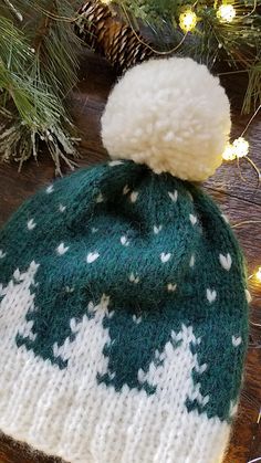 a green and white knitted hat sitting on top of a wooden table next to a christmas tree