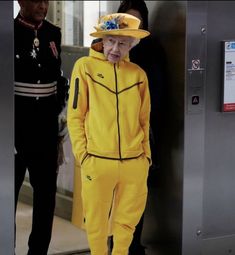 an old man in a yellow suit and hat standing next to a metal door with his hands on his hips