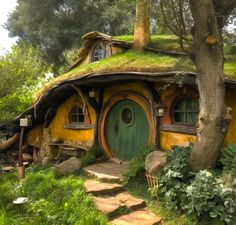 a small yellow and green hobbot house in the woods with steps leading up to it