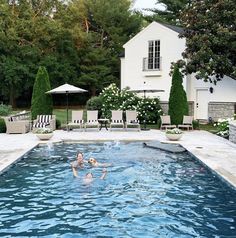 two people are playing in the pool with chairs and umbrellas around it, while another person is swimming