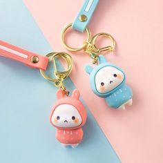 two keychains with cartoon characters on them sitting on a pink and blue surface