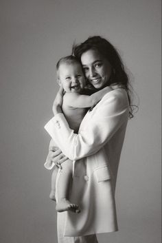 a black and white photo of a woman holding a baby in her arms while smiling at the camera