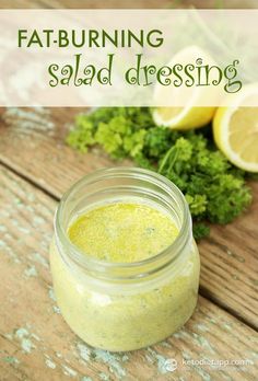 a jar filled with dressing sitting on top of a wooden table next to lemons and parsley