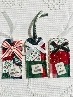 three small christmas gift bags with ribbons and tags attached to them on a white surface