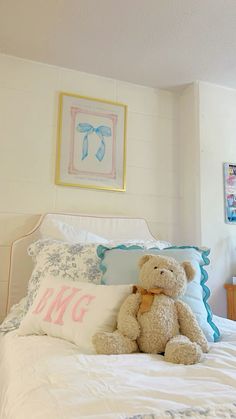 a teddy bear sitting on top of a bed in a room with white sheets and pillows