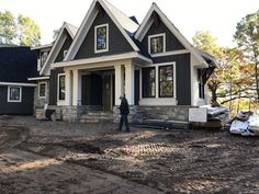 a man standing in front of a house under construction on a dirt lot next to some trees