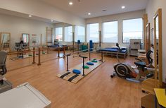 an empty gym room with exercise equipment and yoga mats on the floor, windows overlooking the city