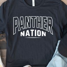 a black shirt with the word panther nation printed on it next to shoes and a pair of jeans