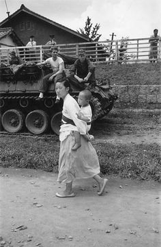 an old black and white photo of people walking in front of a tank