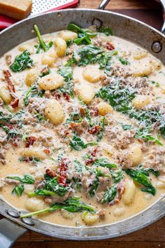 a skillet filled with pasta and spinach covered in gravy on top of a wooden table