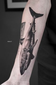 a man's arm with a shark and knife tattoo on the left side of his arm