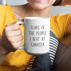 a woman holding a coffee mug with the words tears of the people i beat at canasta