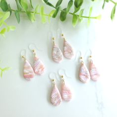 six pink and white marble tear earrings with gold earwires sitting next to green leaves