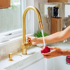 a person washing an apple under a kitchen faucet