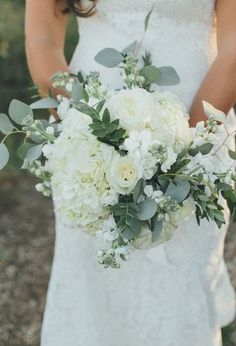 a bride holding a bouquet of white flowers and greenery