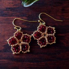 red and gold beaded earrings sitting on top of a wooden table next to a plant