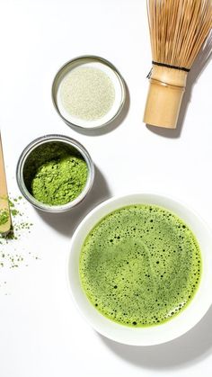 two bowls filled with green powder next to a whisk and wooden spoon on a white surface