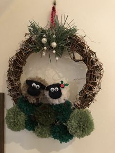 two black and white sheep sitting on top of a wreath hanging from the side of a wall