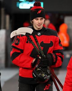 a man in red and black hockey uniform holding a pair of skis while walking down the street